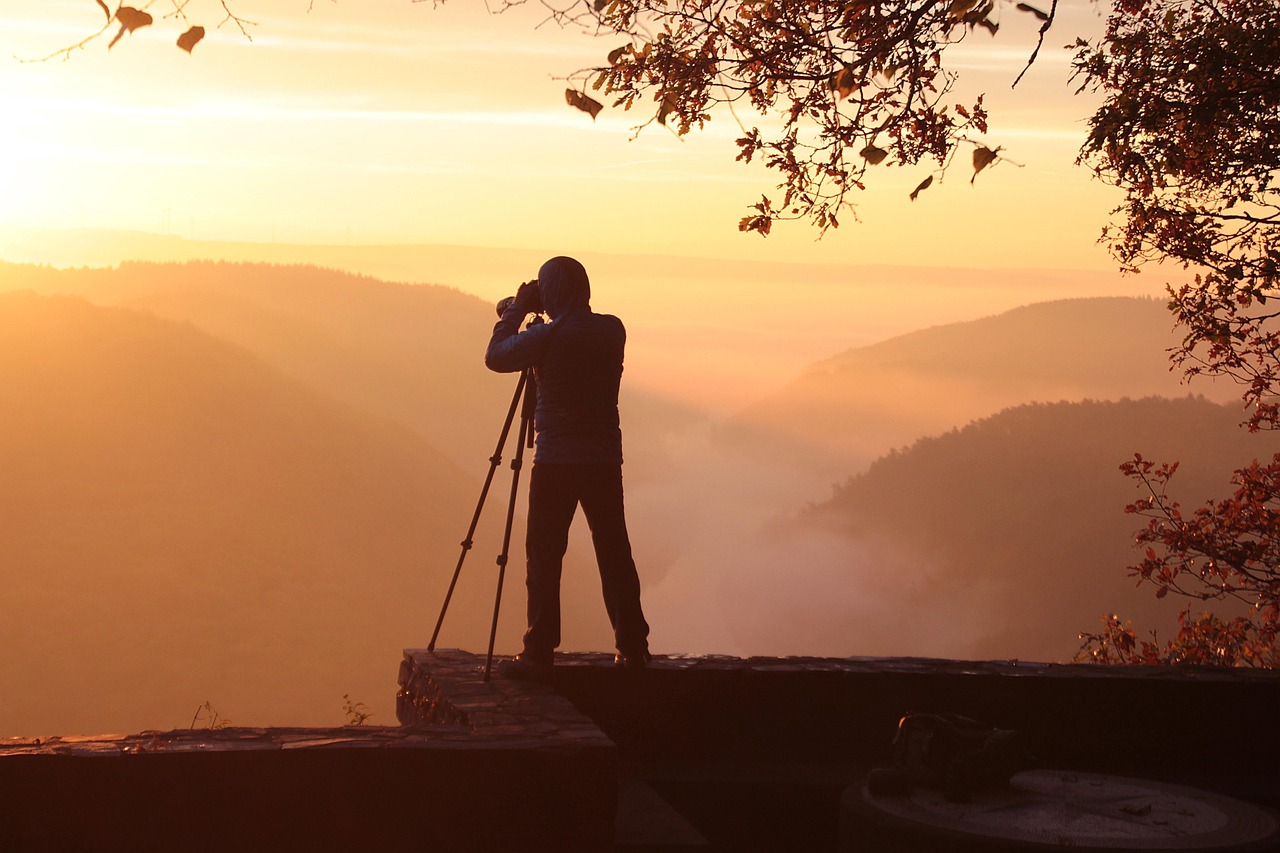 Silhouette of a photographer using a camera on a tripod overlooking misty hills at sunrise